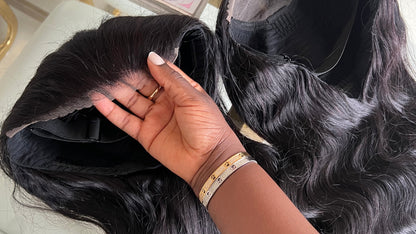 A hand holding a straight wig with transparent lace closure, showing the dark brown hair texture and length.